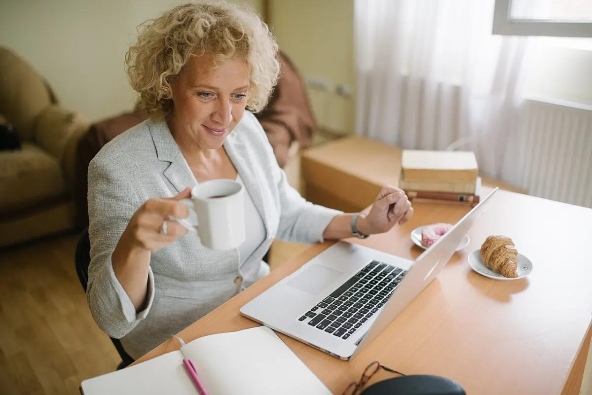 Asset Tracking Software - Elderly woman sitting at her office table and holding a cup of coffee while working on her