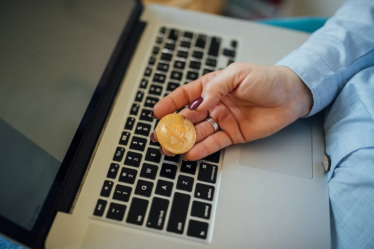 Cryptocurrency Wallet Management System - Close-up of a Bitcoin physical coin in a womans hand and a laptop on her lap
