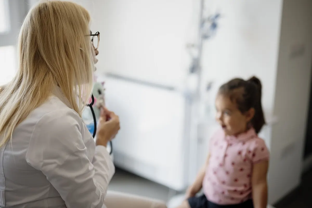 Doctor Appointment Booking System - Doctor talks to a young girl during a consultation in a bright medical office