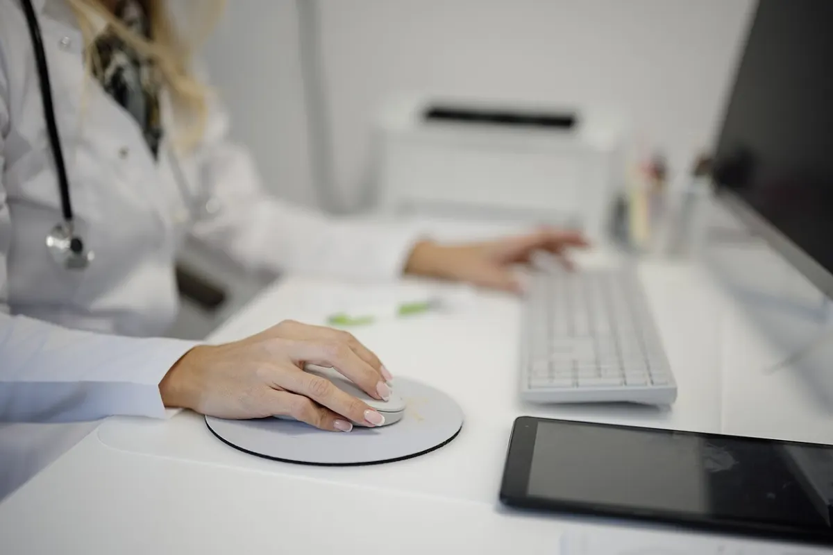 Project Tracking Management System - Doctor working at a desk using a computer mouse and keyboard in a medical office setting