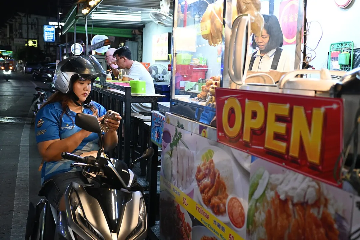 Women Safety App - DZ3 0978 A woman on a motorbike checks her phone while ordering from a brightly lit street