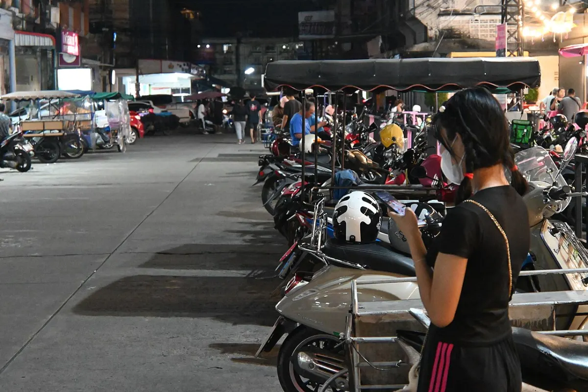 Women Safety App - DFC 2104 A woman wearing a face mask checks her phone while standing beside a row of parke